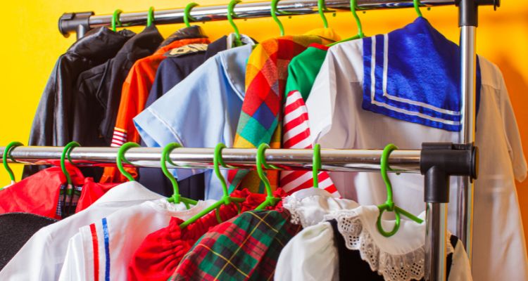A little over a dozen costumes are hung on two silver racks. The hangers are green and the background is a bright yellow.
