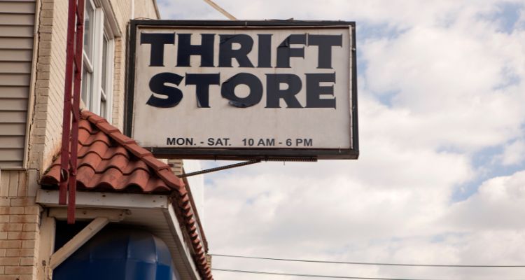 A dilapidated black and white thrift store sign hangs over a shop front. The background is cloudy.