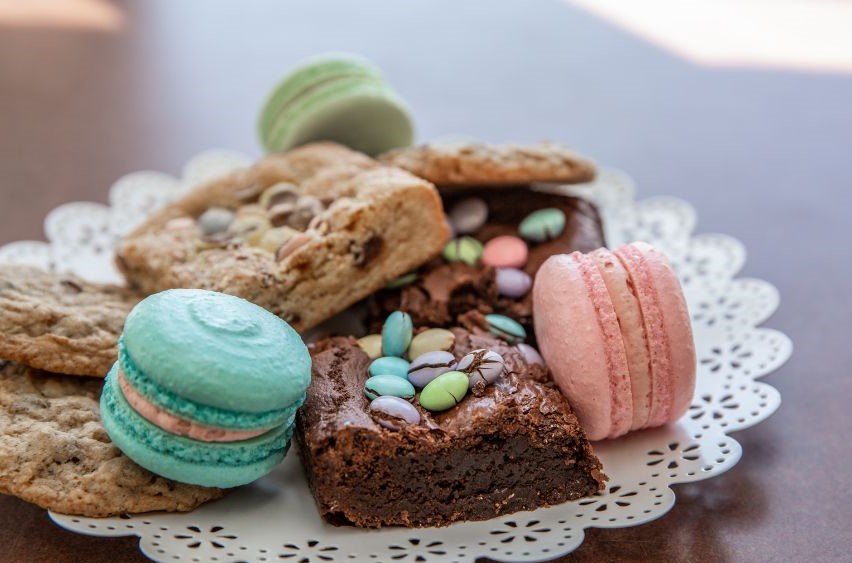 Colorful macarons, brownies, and cookies stacked on a doily on a plate