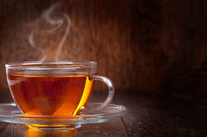A clear cup of what looks like tea steaming and sitting on a saucer