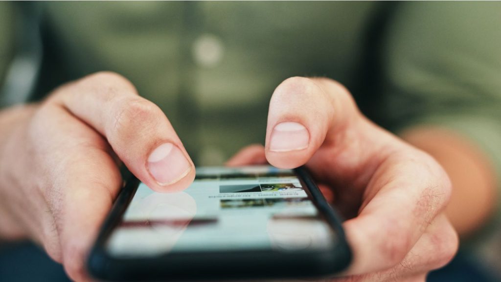A person in a green shirt is on their phone, thumbs typing something.
