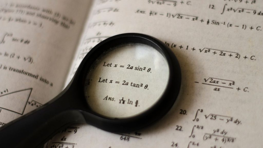 A page from a math textbook with equations on it. A magnifying glass focuses in on one.