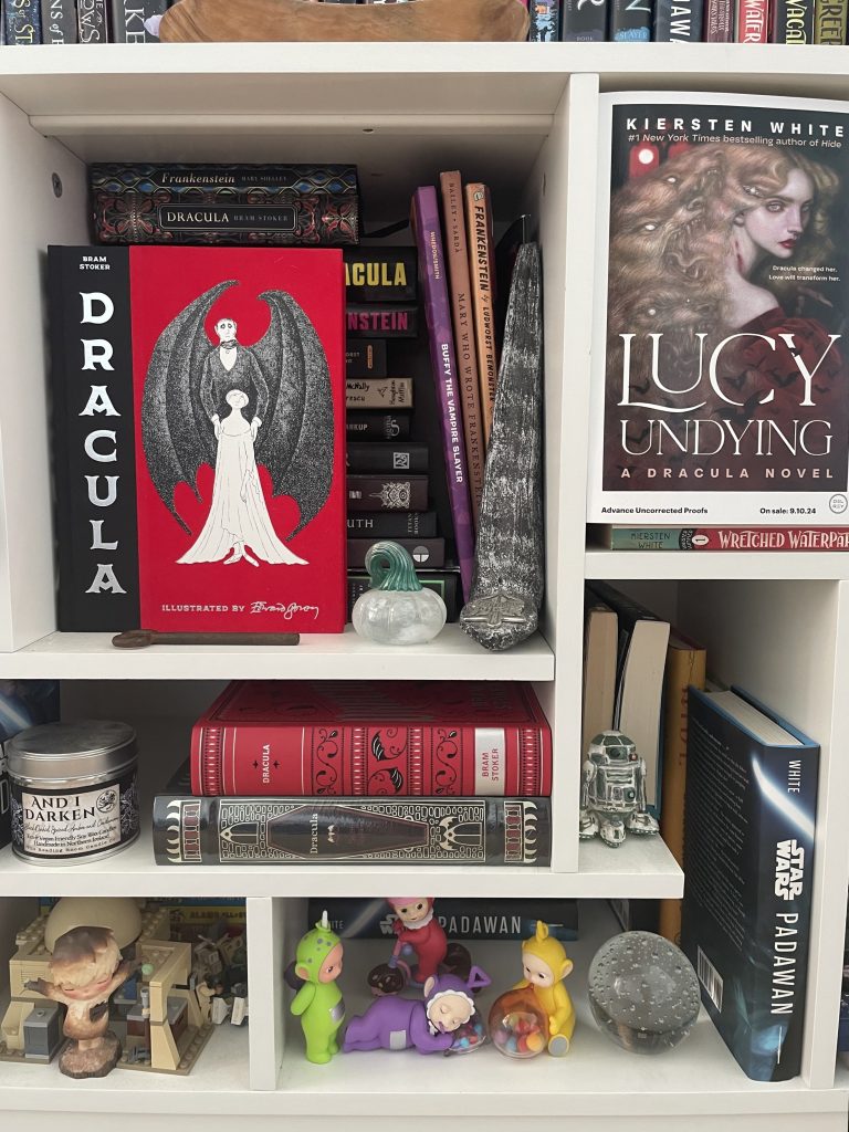 Another close look at her bookshelf featuring the book Dracula and her new book Lucy Undying: A Dracula Novel at the front, focus on those two.