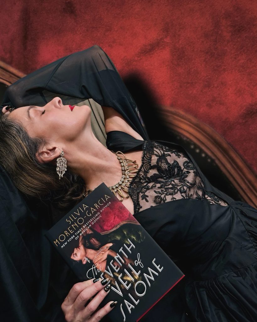 Carmen wearing a black dress and holding The Seventh Veil of Salome by Silvia Moreno-Garcia