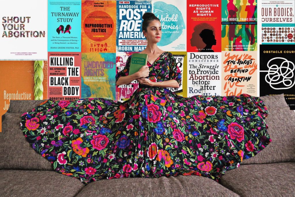 Carmen sitting and holding a book with book covers in the background