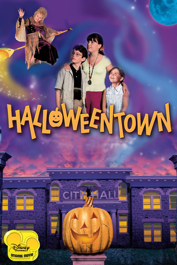 The main characters of Halloweentown appear above the title, set against a purple city hall with a large carved pumpkin in the foreground. All characters gaze up at a witch flying on a broomstick in the sky.