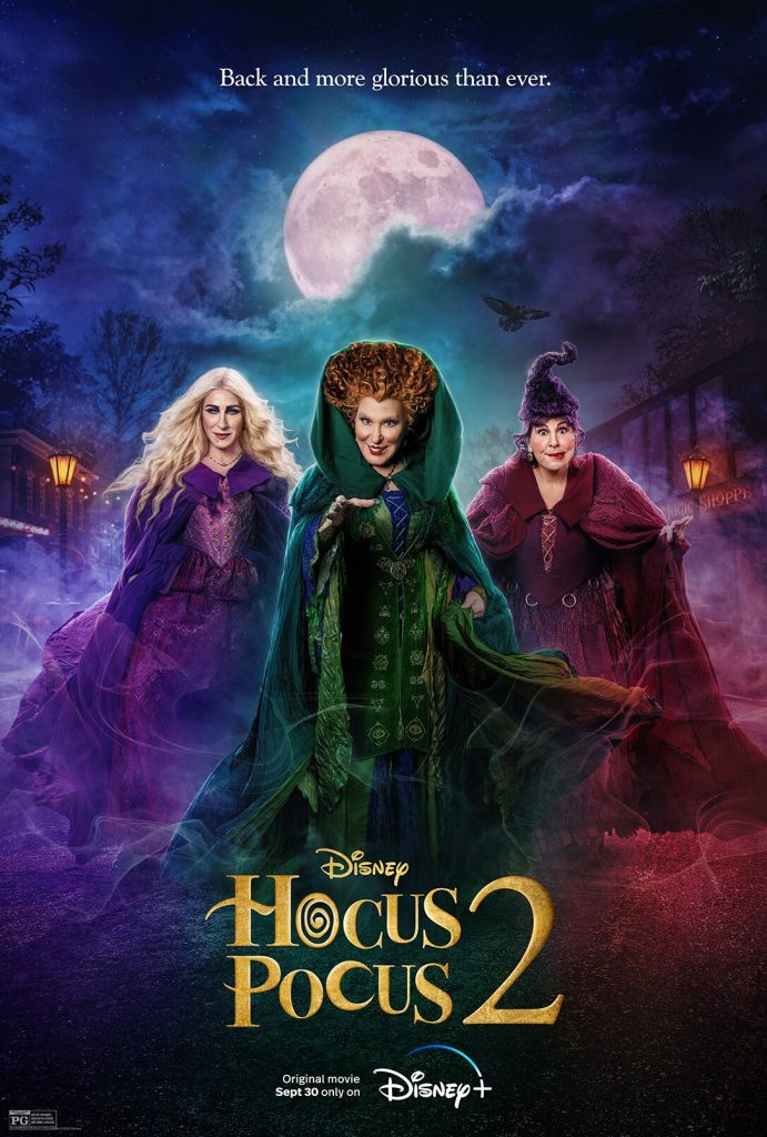 The Sanderson sisters stand amidst swirling purple, green, and red mist, with a full moon shining in the sky and a small town in the background.