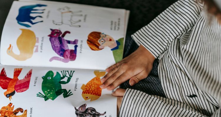 A person wearing a striped shirt is reading a book with colorful images inside it.