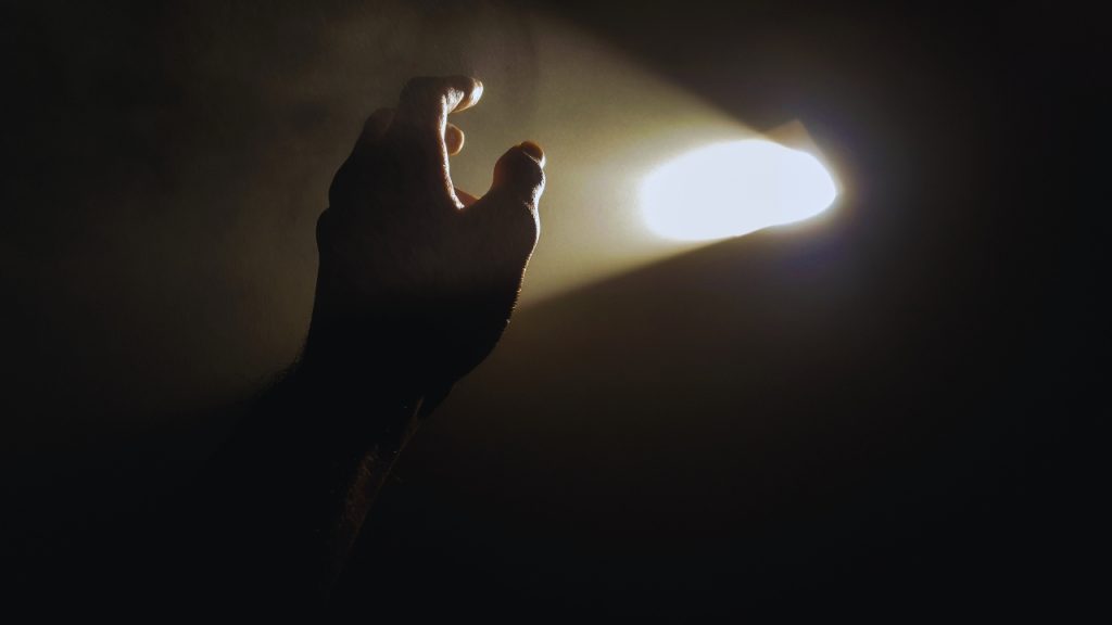 A hand in a dark space reaches up towards a sliver of light.