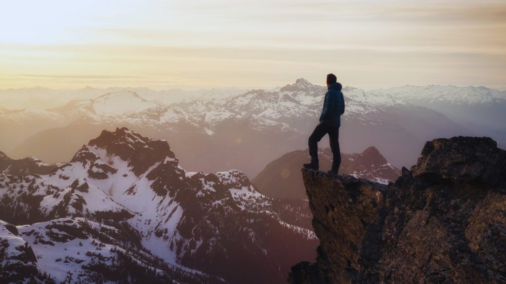 A man standing on a mountain facing the sunset.
