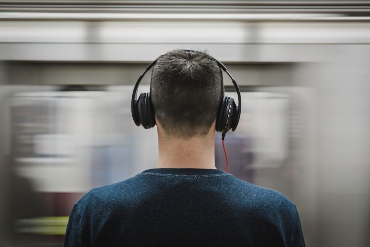 A man wearing headphones standing in front of a moving tube or subway.