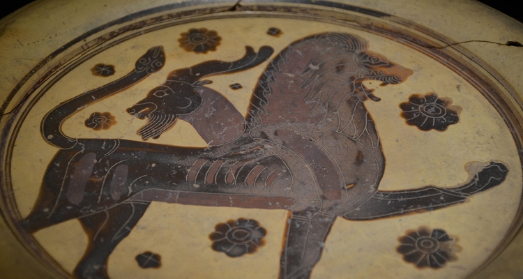 A close-up photo of an old ceramic plate depicting a brown creature with a lion's head, a goat's body (and an extra goat's head), and a snake's tail.