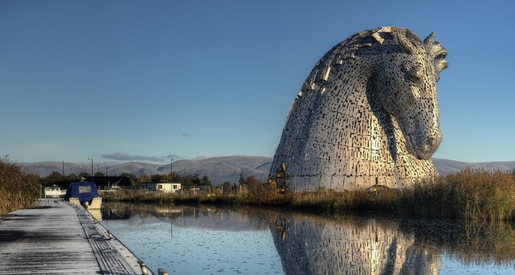A photo of a giant metal statue of a horse's head overlooking a lake and small town.