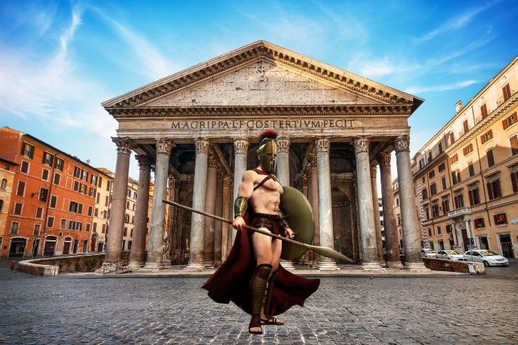 A spartan soldier waits outside an ancient Greek building.