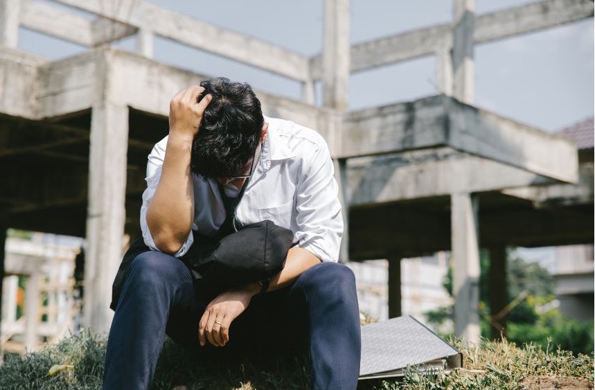 A man sitting on the ground with a hand in his hair looking stressed