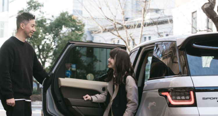 A man holding open a car door for a woman. They are both smiling.