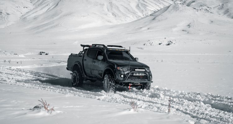 A black truck driving across the snow.