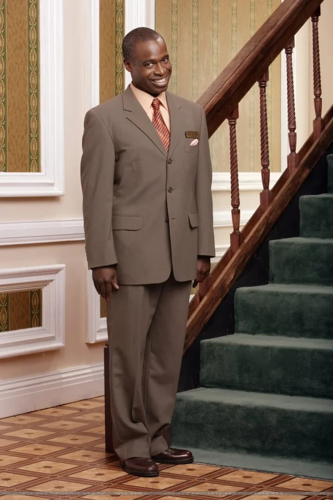 Mr. Moseby smiling and standing near a green carpeted staircase. He is wearing a brown tux.