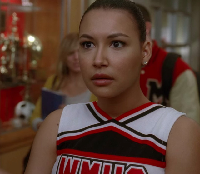 Santana in her cheer uniform staring wide-eyed at something off camera in slight shock.