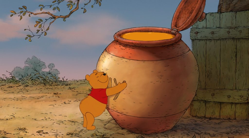 A yellow bear wearing a red shirt hugs a big jar of honey. The sky is blue in the background.