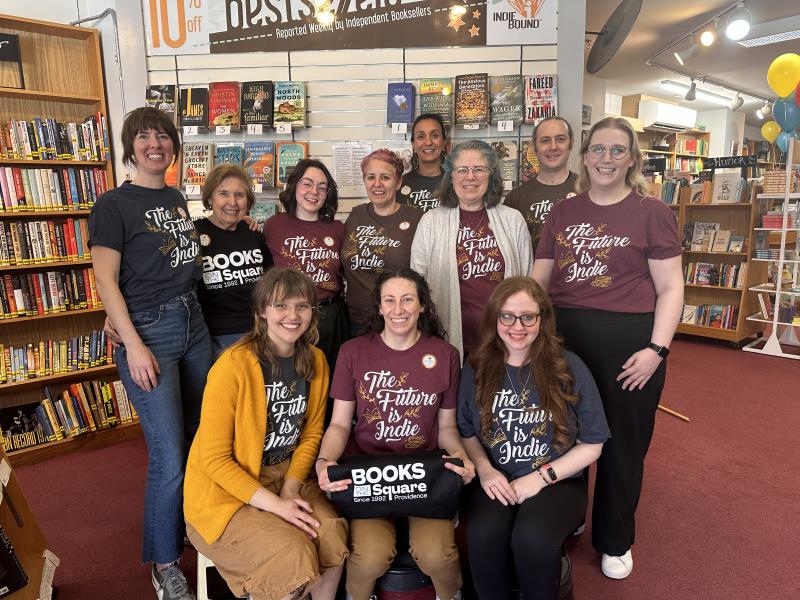 The 11 staff members of Books on the Square smiling, with one holding a small sign with the store's name.