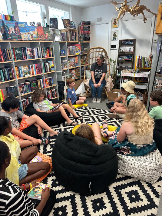 A group of children and a woman sitting in a circle and reading.