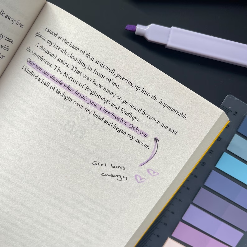 A page of a book is shown and a line of text has been highlighted in muted purple. An annotation says "Girl Boss energy". A highlighter and colorful tabs accompany the book.