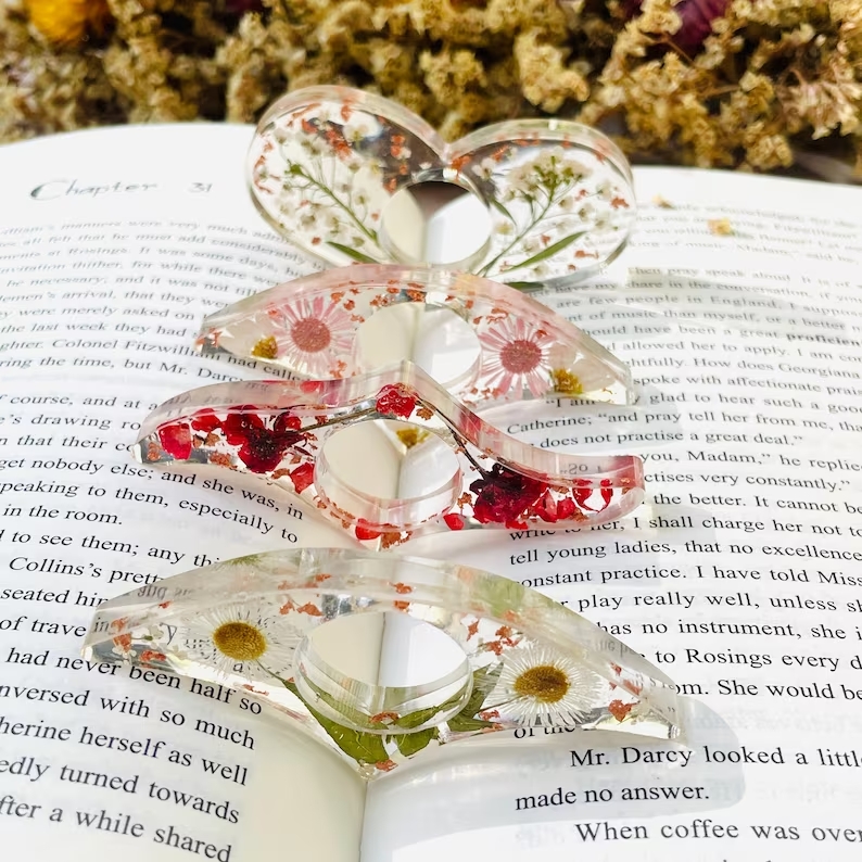 Four transparent page holders are sitting between the binding of a book. They have different kinds of pressed flowers in them.