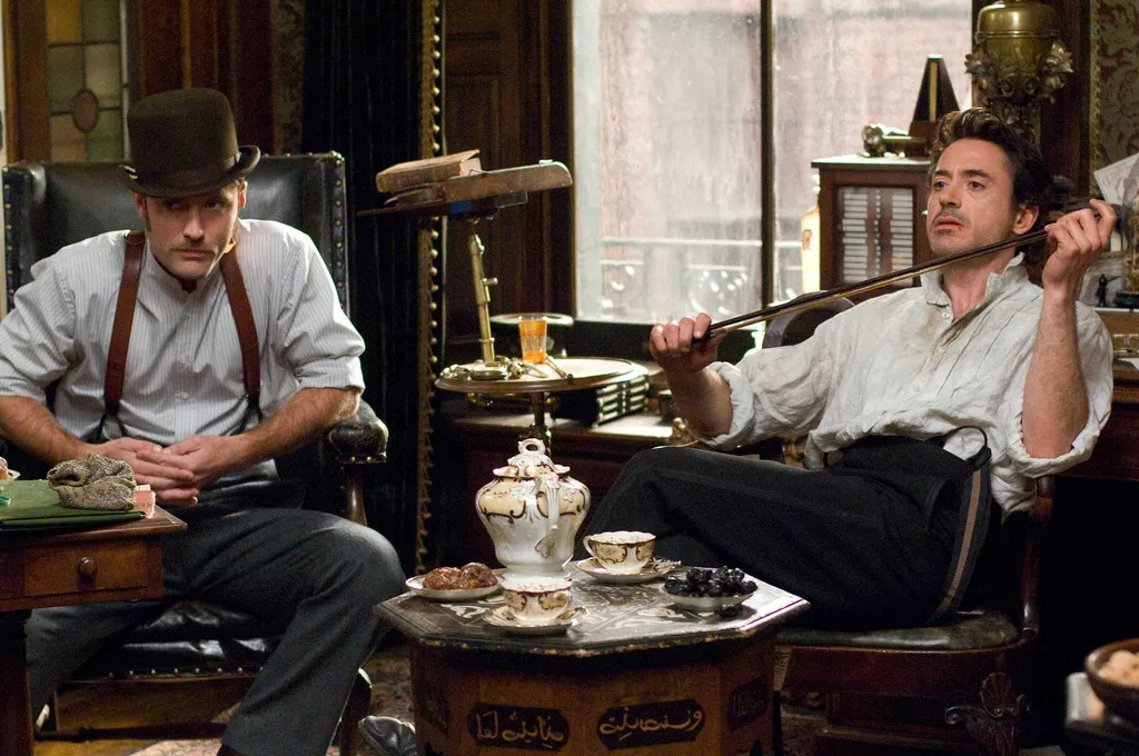 Sherlock and John from the 'Sherlock Holmes' movie with Sherlock lounging in a chair and John hunched over in his