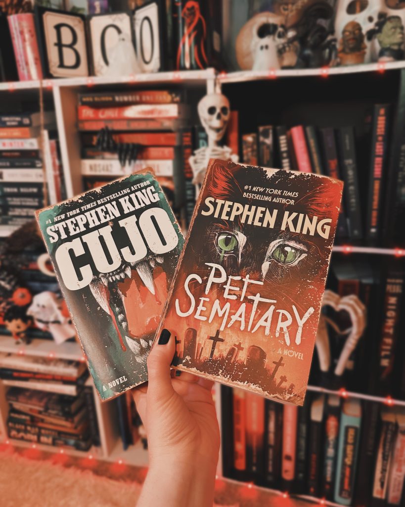 Hand holding two books, Cujo and Pet Sematary, in front of a bookcase