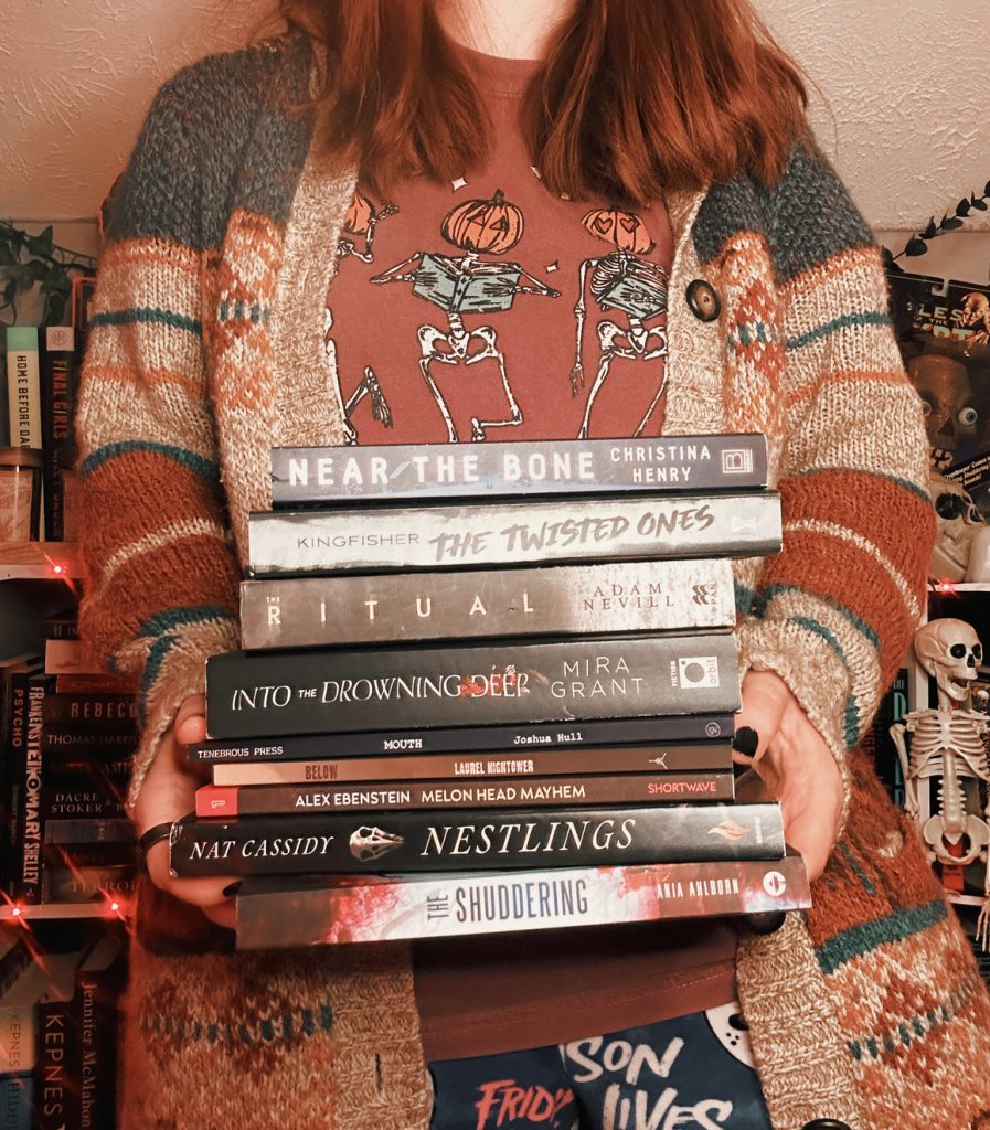 Woman wearing a sweater and a skeleton shirt holding a stack of books