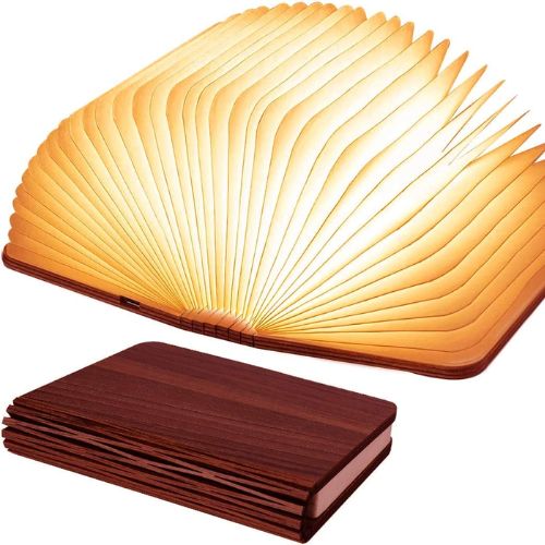 Two identical wooden book lamps over a white background. The top lamp is unfolded to reveal glowing pop-up pages, while the bottom lamp is shut and is made of dark brown wood.