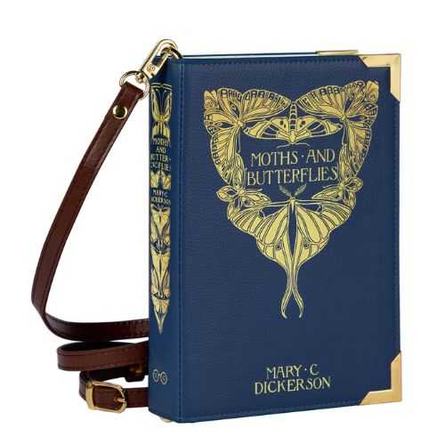A rectangular purse standing on its side over a white background. The purse, which looks similar to a hardcover book, is dark blue with gold accents and reads, "Moths and Butterflies" as well as, "Mary C Dickerson". The top text is surrounded by illustrated golden moths and butterflies, as is the spine of the purse. The purse is connected to a brown over-the-shoulder strap.