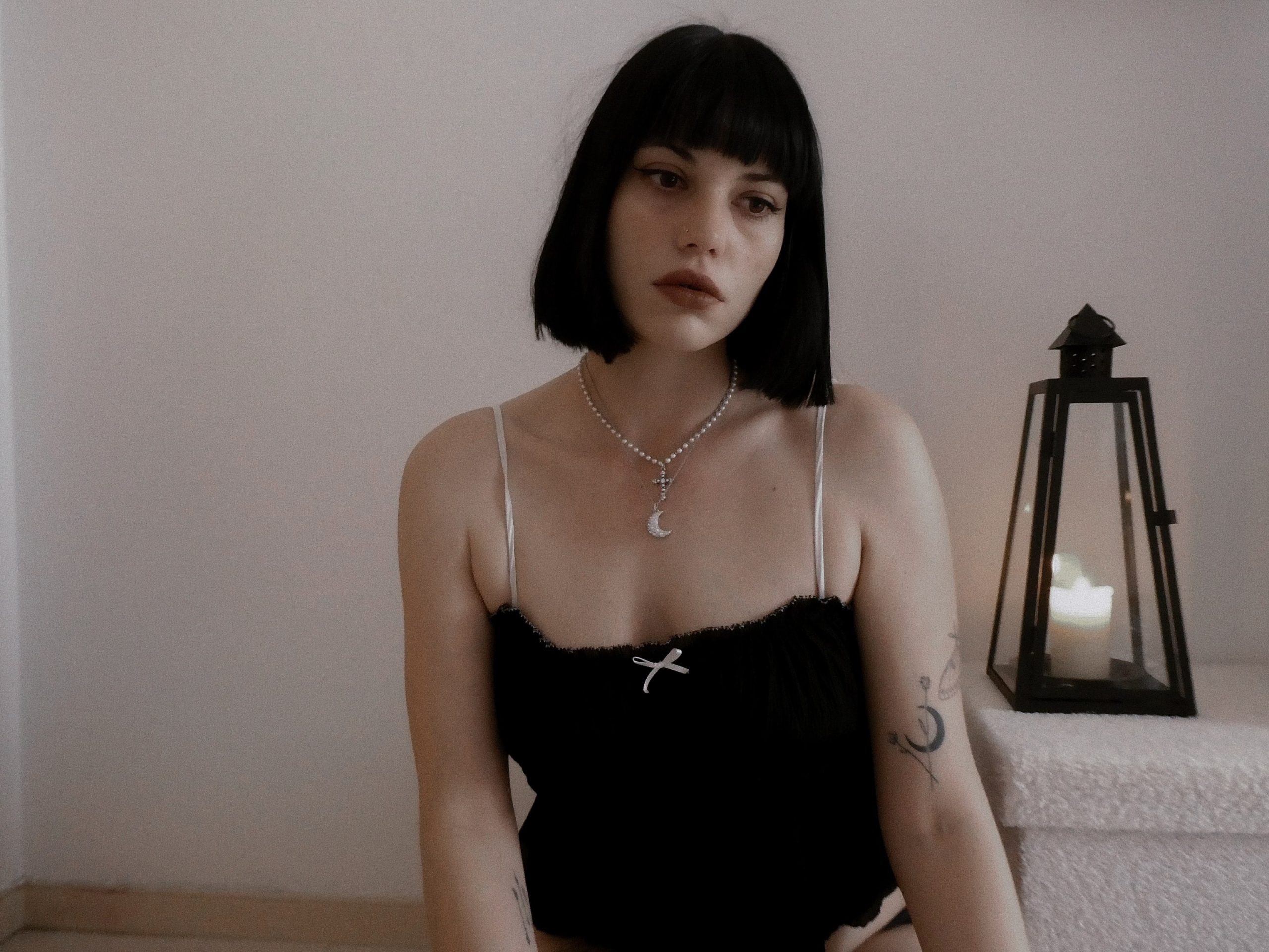 Vicky dressed in all black and a moon necklace with a silver headpiece while holding a lit dark red candle.