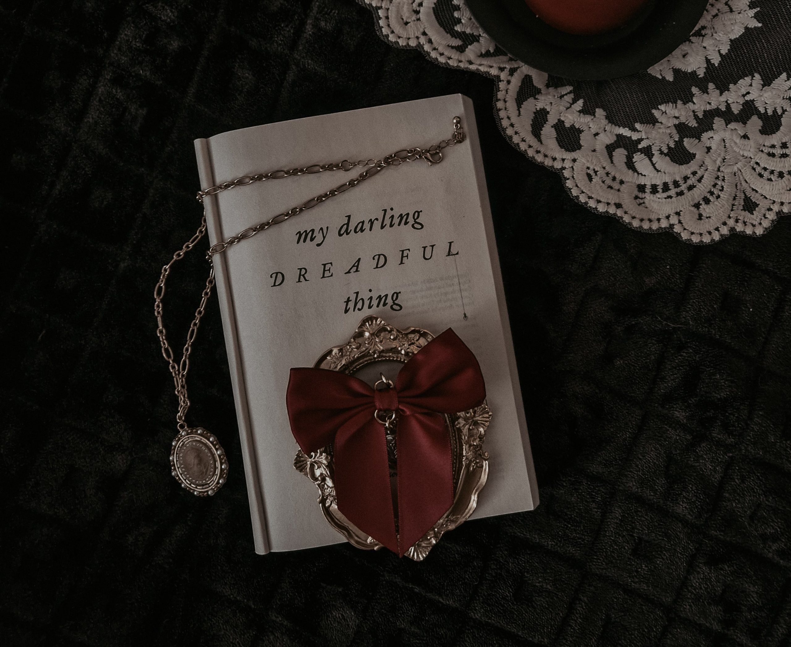 Photo from Vicky's feed showing the book "My Darling Dreadful Thing" turned open to the inside title page with a locket draped over it and a dark red bow placed on top.
