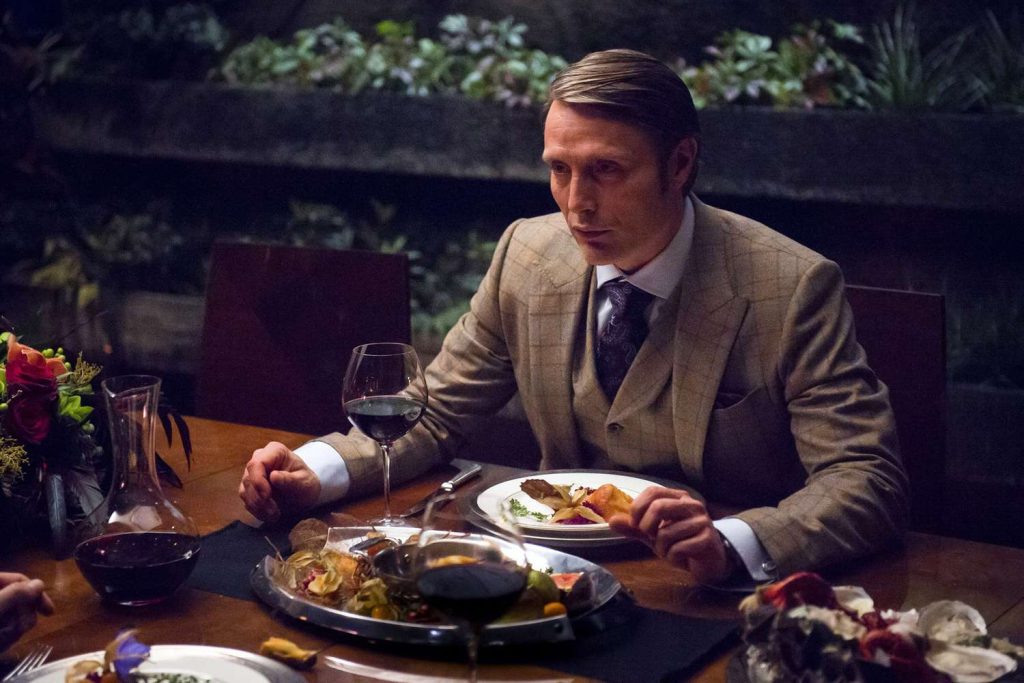 "Hannibal" TV still of Hannibal eating a luxurious dinner with what's presumably human organs with wine.