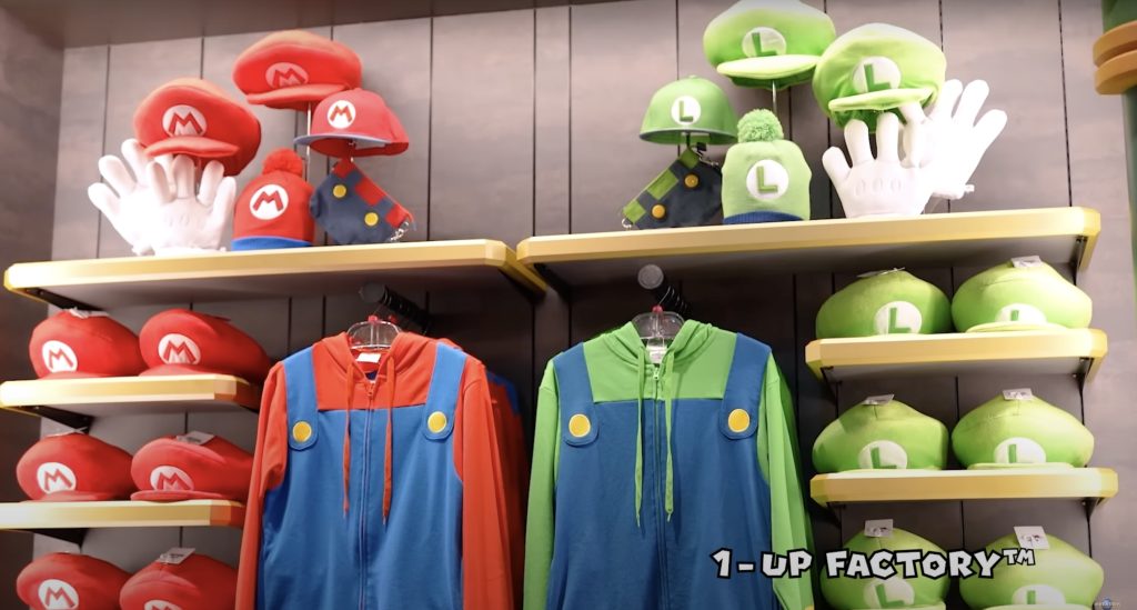 Wooden shelves hold up Mario jackets, hats, and gloves on one side and Luigi jackets, hats, and gloves on the other.