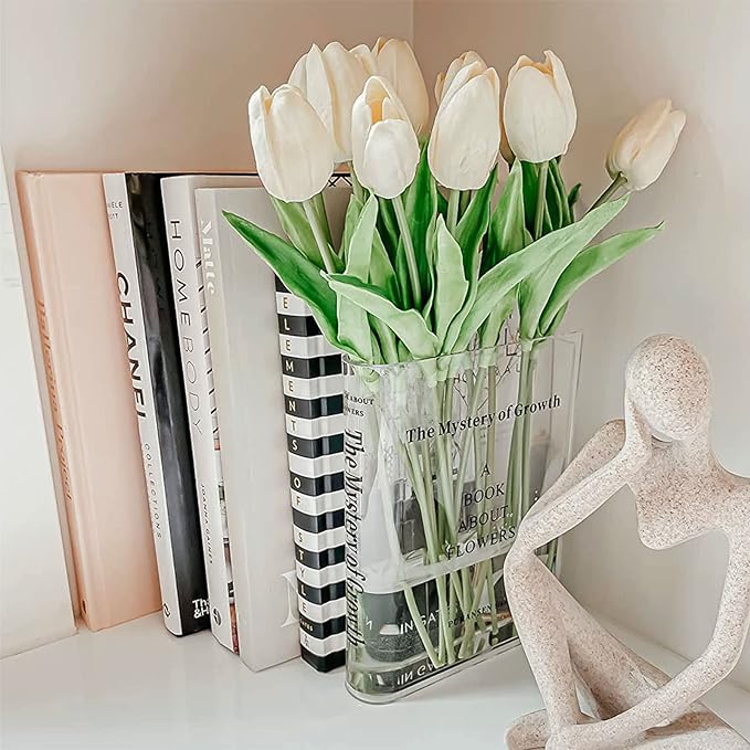 White background aesthetic with a flower vase in the shape of a book with white tulips inside on a bookshelf.