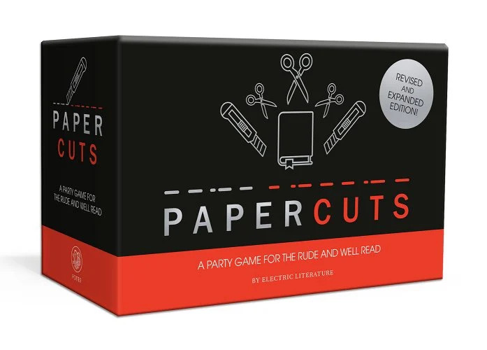 A black-and-red card game box with scissors, a book, and box cutters on the front.