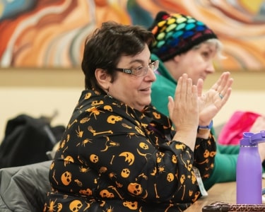 Two people, one wearing black and one wearing green, watch something outside of the image while clapping.