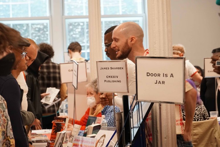 Multiple people standing, buying and selling books while conversing with each other.