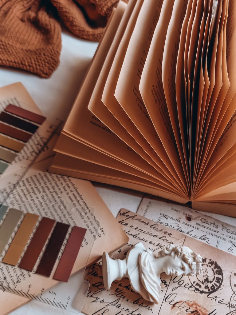 A fanned-opened book sits on a bed with small book markets and a tiny Greek bus beside it.