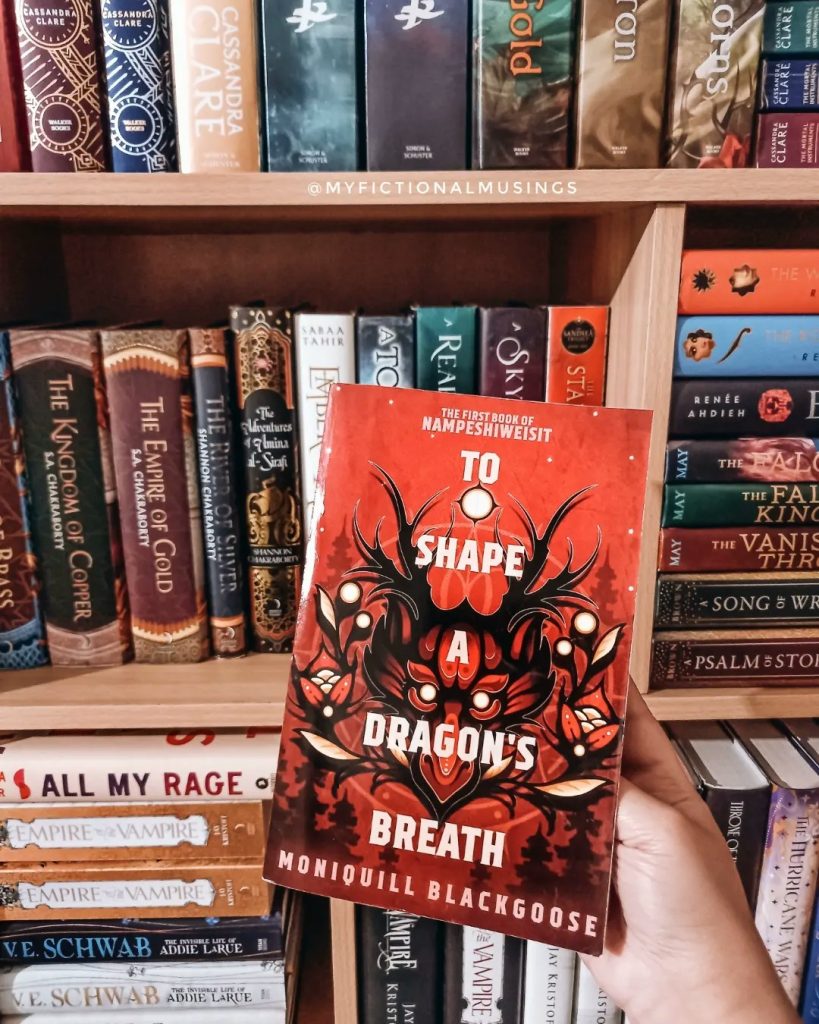One of the books mentioned is held in front of a filled bookshelf.