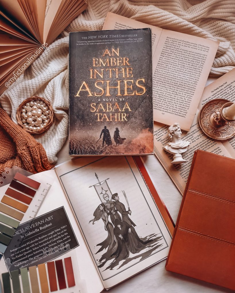 A book from the Ember in the Ashes series sits on top of other opened books and blankets.