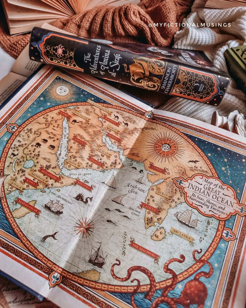 An antique-style map of the Indian Ocean and the surrounding lands is in a book. Other books surround it as they are placed over multiple cozy blankets.
