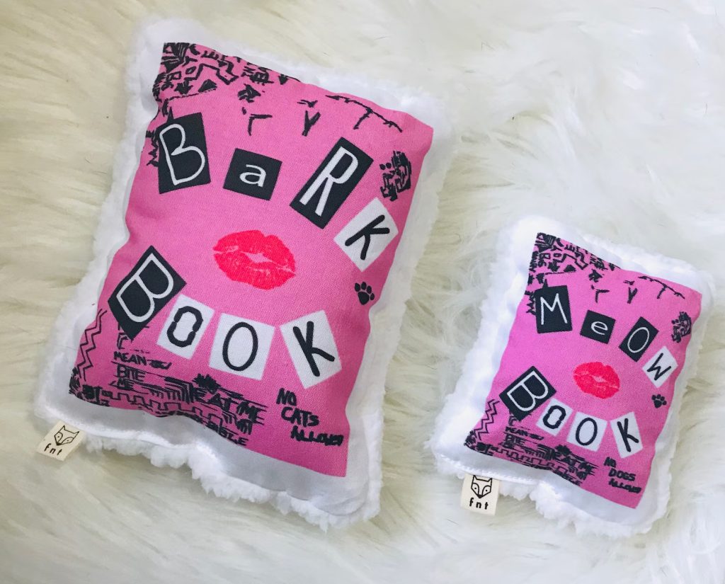Two "Burn Books" from "Mean Girls" bright pink. One big chew toy saying "Bark Book" with a smaller one saying "Meow Book."