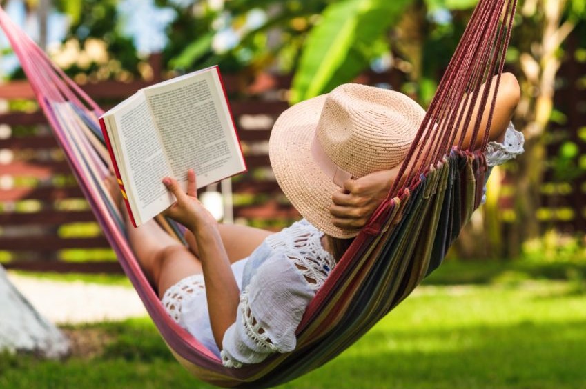 Someone reading a book while lying in a hammock