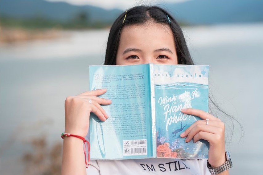 A woman holding up a book with an illustrated cover of a person diving in the ocean