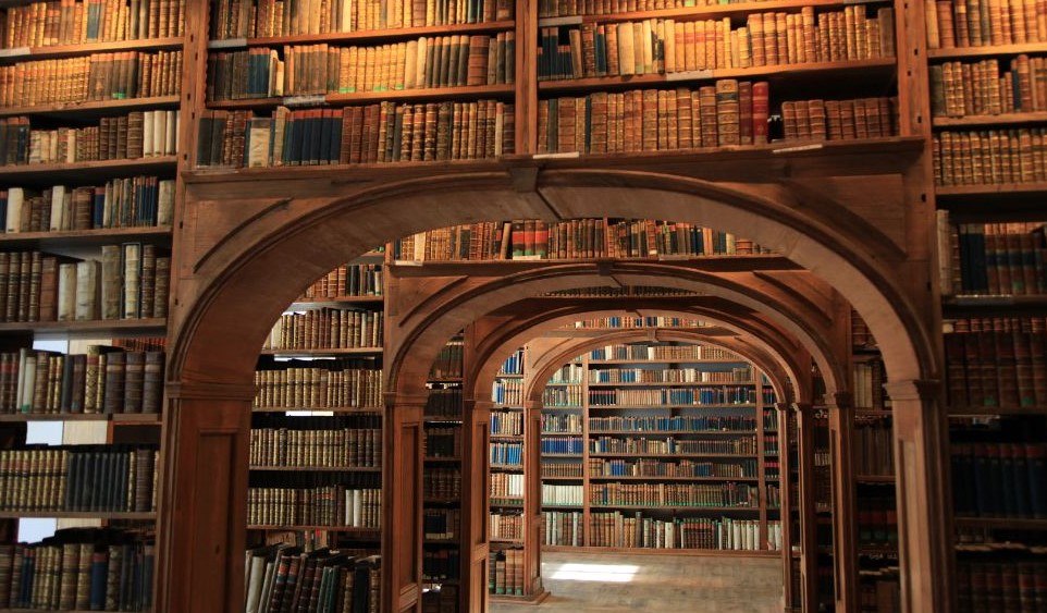 A library with bookshelves going around arches and full of books