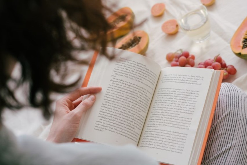 Someone reading a physical book with fruit in front of them